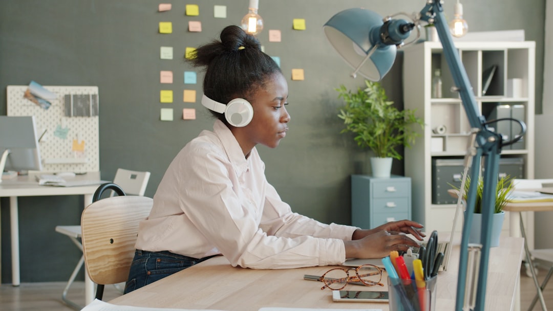 joyful mixed race girl working with laptop typing then dancing wearing headphones in office. Entertainment and workplace conc
